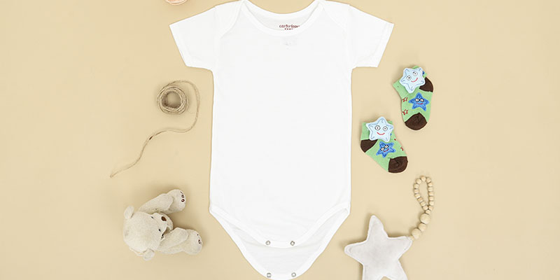 Baby romper, socks, teddy bear, and star toy layed out on a flat platform
