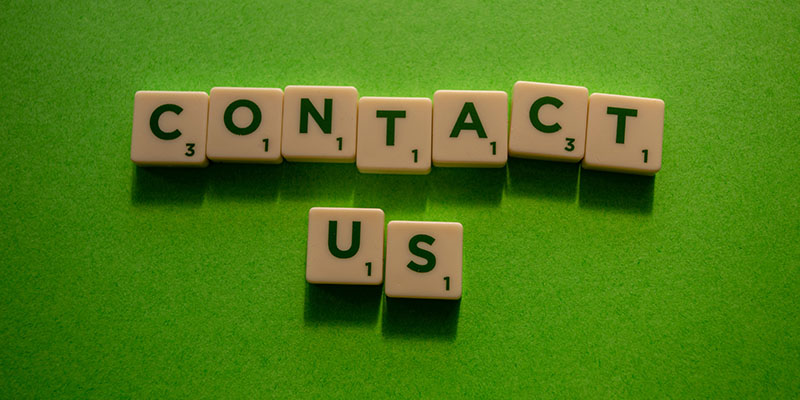 Scrabble Letters spelling out Contact Us against a green background