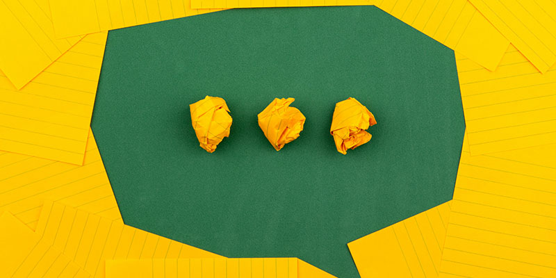 three crumpled yellow papers on green surface surrounded by yellow lined papers