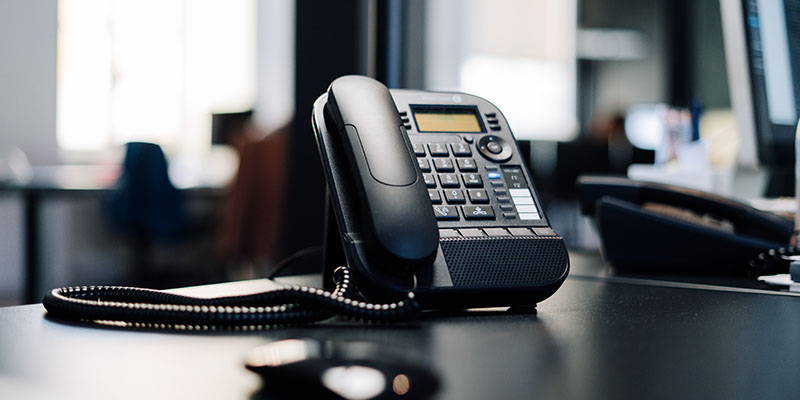 Black landline phone on a black wooden desk