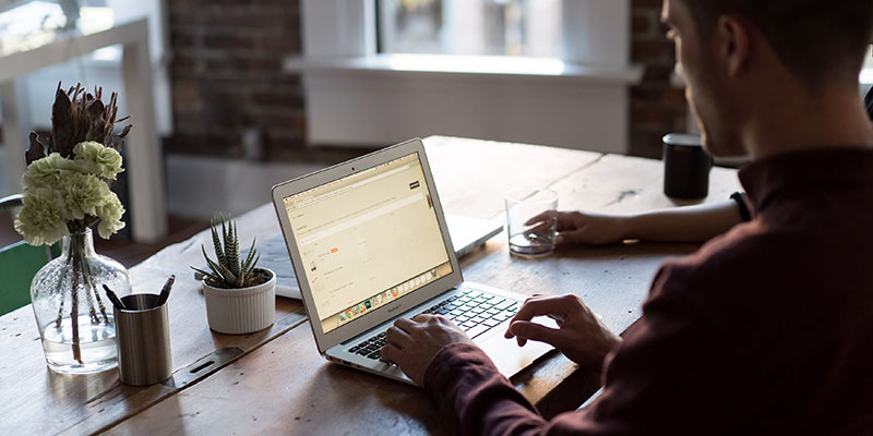 Man operating a laptop on a wooden table