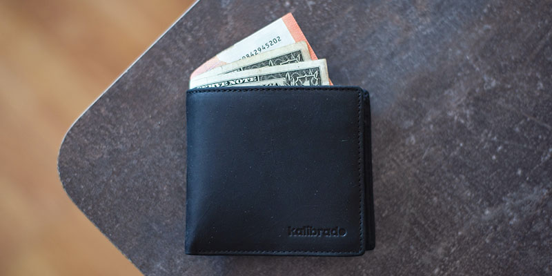 Black leather wallet with some dollar bills sticking out