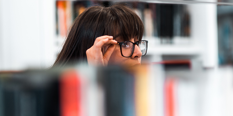 A woman wearing black specs checking books in a library