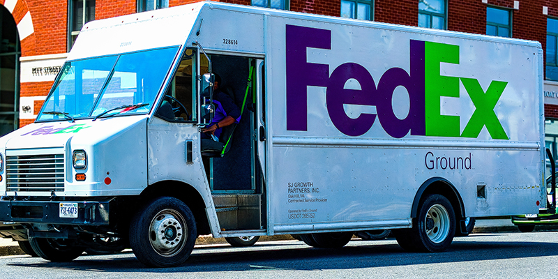 A White FedEx truckw with delivery man inside, parked outside of an office building in Washington DC on a sunny day.
