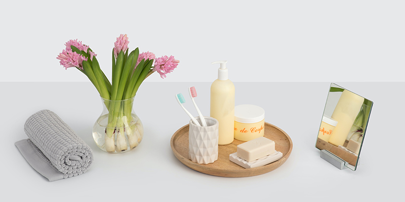 Towel, vase with flowers, mirror, soap, toothbrush, moisturizer, and cream on a white table 