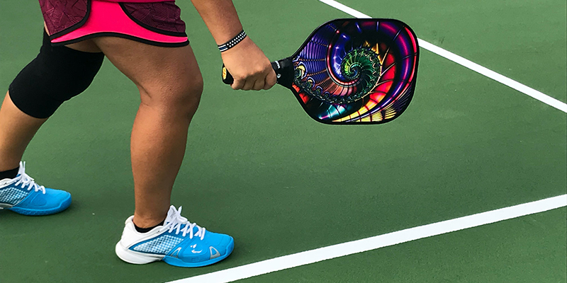 A woman wear a pink outfit with blue shoes playing pick playing on a green court.