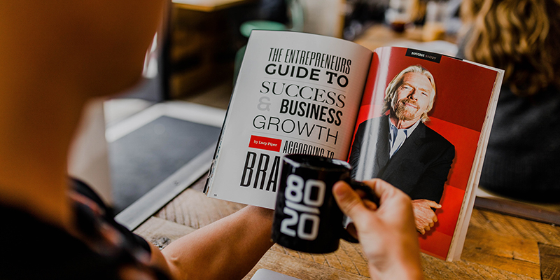 A man reading a magazine featuring Richard Branson while sipping coffee