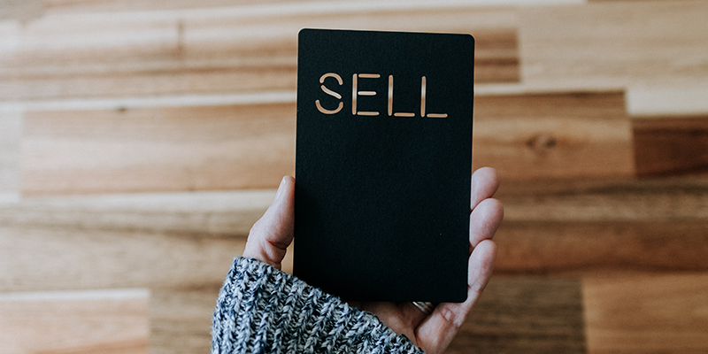 A hand holding a black card that says sell 