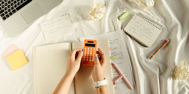 Person Holding Orange and White calulator over a math book