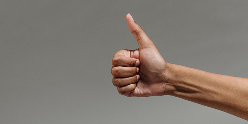 A person doing thumbs up on a grey background