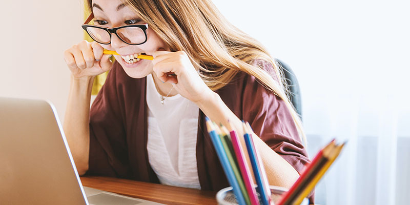 A woman nervously chewing on pencil while working on her laptop.