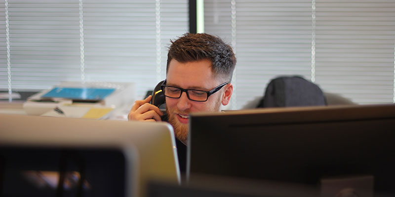 A man answering a phone on his office desk