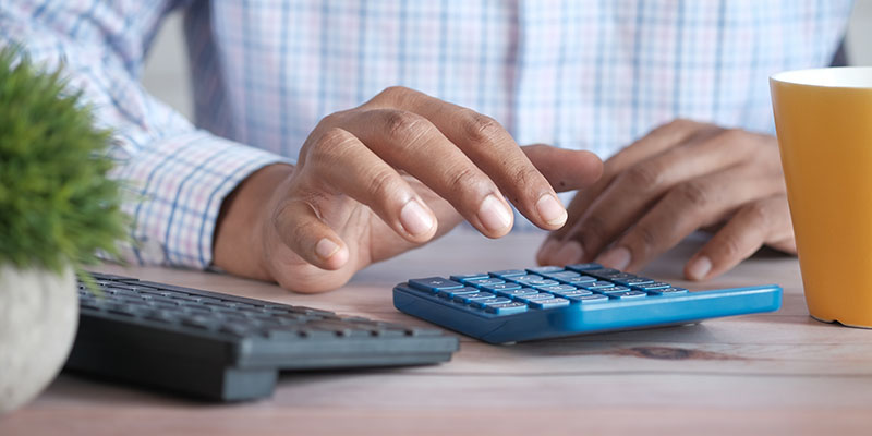 A man using two calculators on a brown desk