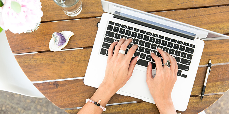 Two hands typing on a laptop placed on a wooden bench