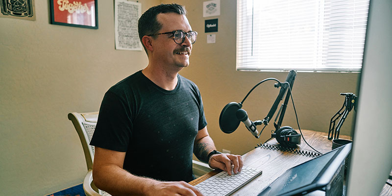 A man wearing a Black tee creating a podcast episode in his room