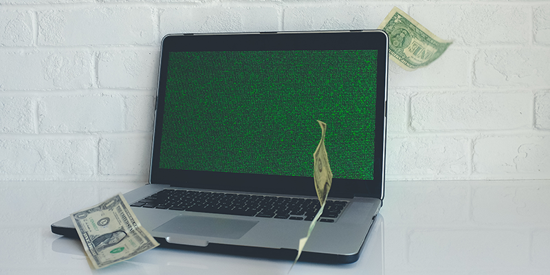 A greyish black laptop with a green screen and dollar bills flying around it