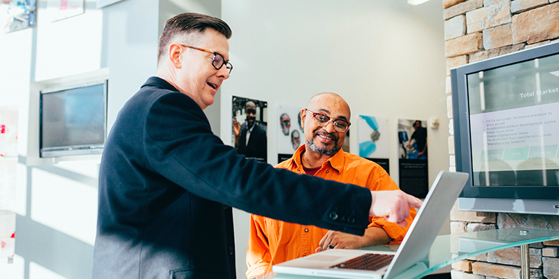 A salesman pointing to a screen and explaining the product to a business owner wearing an Orange shirt