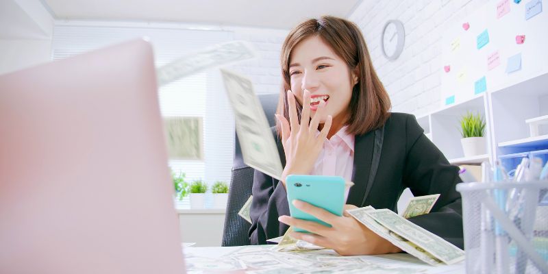Woman looking at a computer screen surrounded by dollar bills
