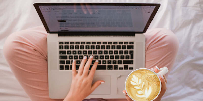 A woman typing on her laptop while drinking coffee