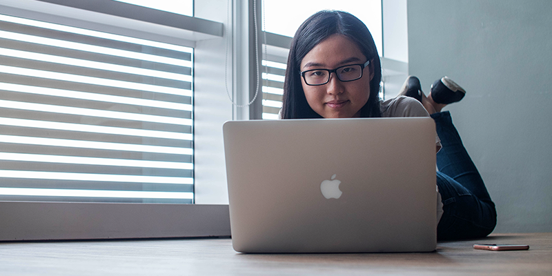 A teen using a silver macbook-beside clear glass window