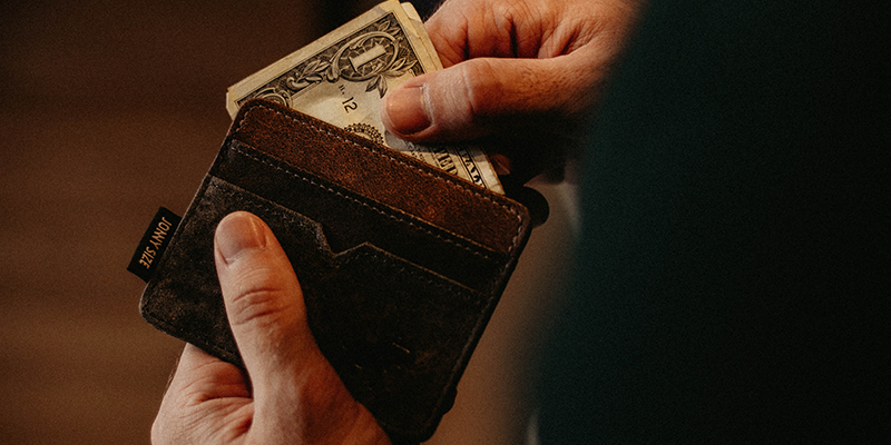 A hand removing dollar bills from a brown wallet
