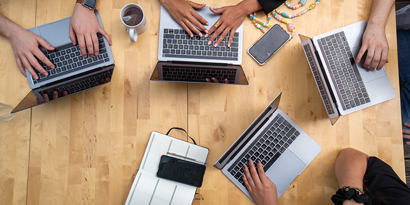 A wooden table with multiple people sitting around and working on their laptops