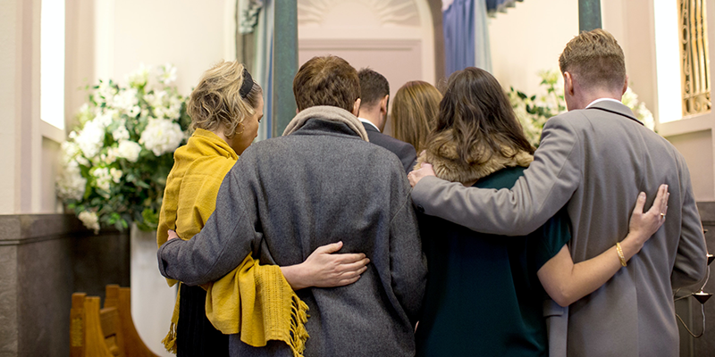 A group of people comfort each other at a funeral ceremony in a crematorium chapel